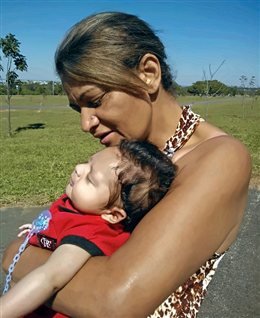 A Célia segurando o João ainda bebê, cochilando no colo dela ao ar livre